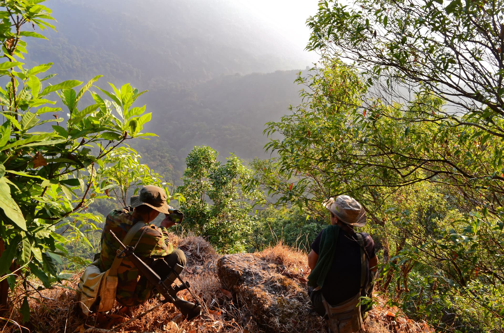 Two people looking out over forested mountains at first light in Kawthoolei